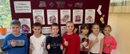 Uczniowie stoją przed gazetką tematyczną związaną ze Światowym Dniem Zespołu Downa, podnoszą kciuka w góry