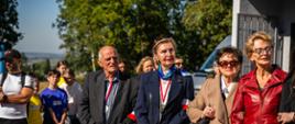 Kombatanci i Wicestarosta Powiatu Proszowickiego przed wręczeniem nagród w biegu, w tle zawodnicy biegu
