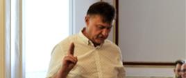 Gerard Nickel mężczyzna w średnim wieku ślubuje w czasie sesji Rady Gminy Świerklaniec, która odbywa się w jednej z sal w Pałacu Kawalera. Jedną rękę ma uniesioną w geście ślubowania. Spogląda na kartkę papieru, z której odczytuje treść ślubowania do ustawionego przed nim mikrofonu.