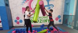 Uczeń z uczennicą biją się gąbkowymi belkami w basenie z miękkimi gąbkowymi klockami
