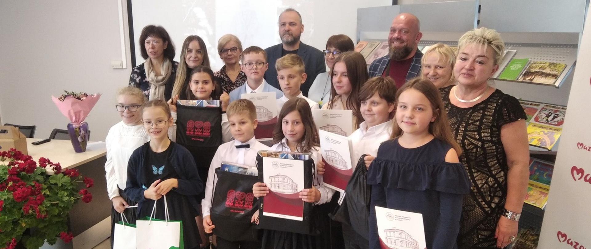 Na zdjęciu laureaci konkursu oraz Jury. Dzieci w dłoniach trzymają dyplomy oraz torby z nagrodami ufundowanymi przez sponsorów.