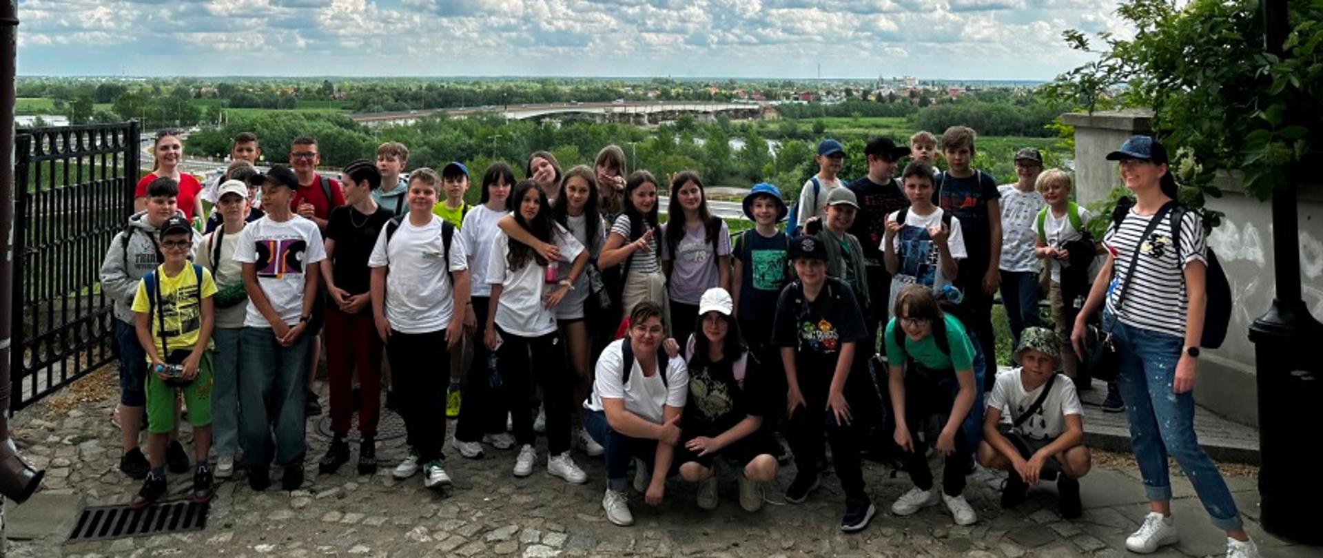 Grupa młodzieży stojąca obok siebie. Za nimi rozciągająca się panorama.