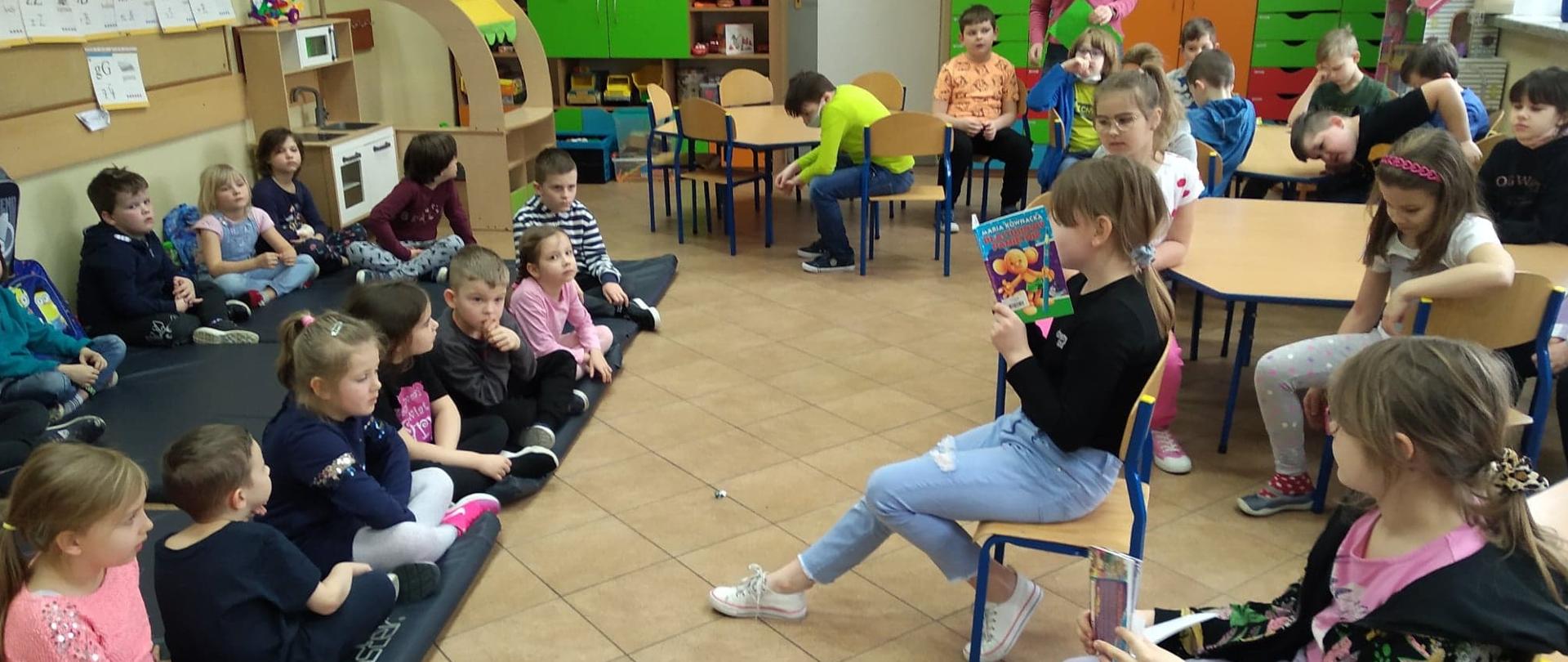 Dzieci po jednej stronie sali siedzące na matach na podłodze a na przeciwko nich inne siedzące 