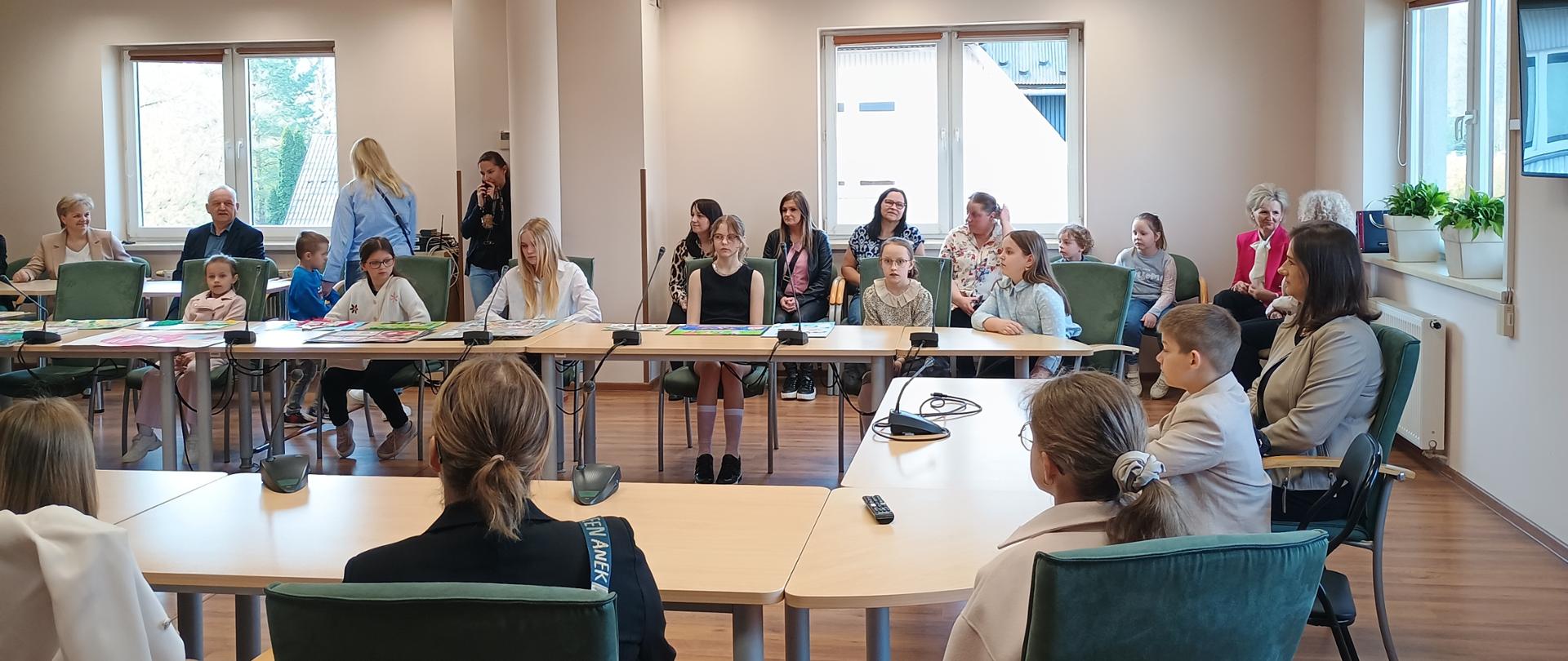 Dzieci z rodzicami siedzą za stołem w radzie gminy
