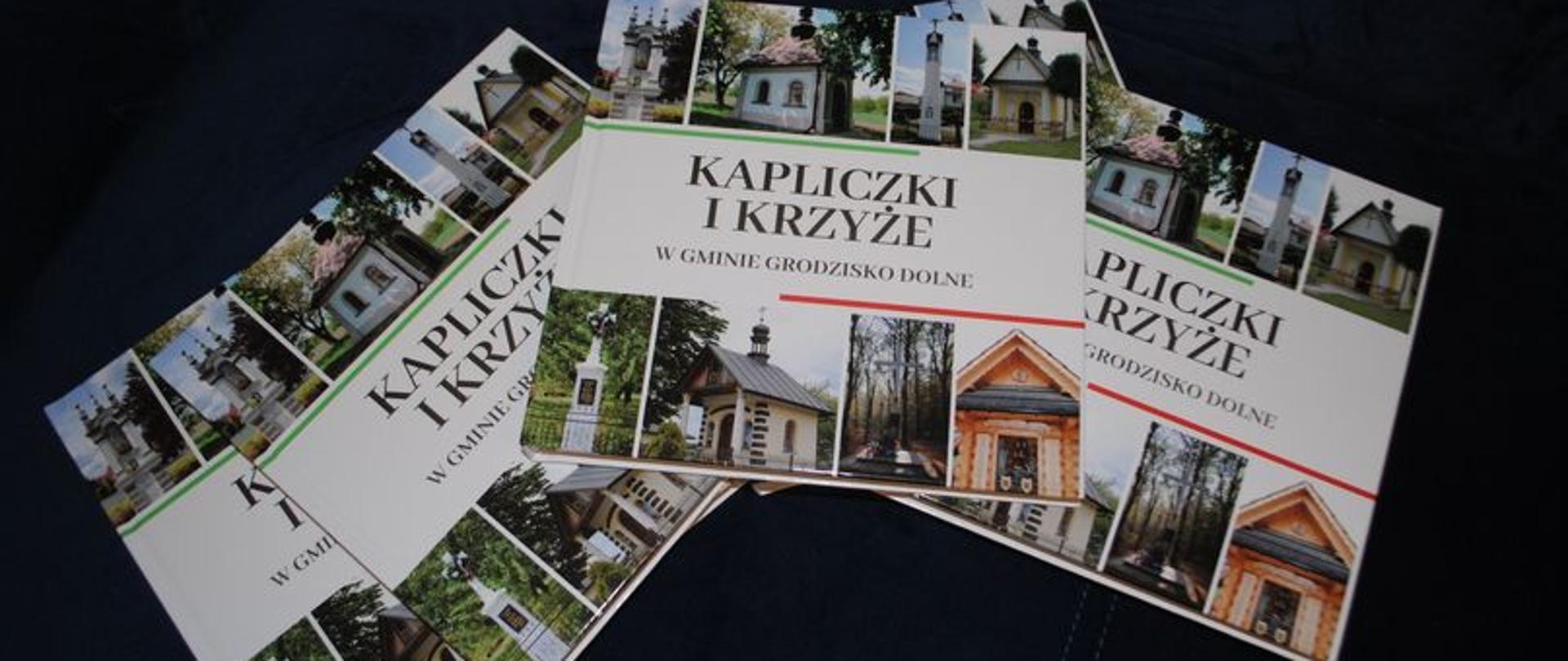 Zdjęcie przedstawia cztery foldery leżace obok siebie na czarnym tle. Foldery są o kapliczkach i krzyżach w gminie grodzisko Dolne 