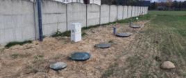 Zdjęcie przedstawia wkopane zbiorniki przydomowej oczyszczalni ścieków, w tle znajduje się betonowy płot.