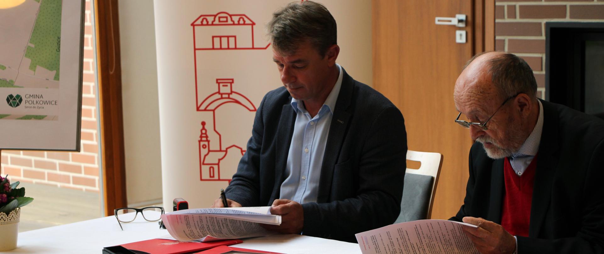 Dwóch mężczyzn siedzących przy stole , podpisujących dokumenty. 