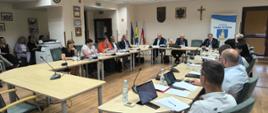 Sesja Rady Gminy 26.06.2025r., zdjęcie sali obrad podczas trwania sesji. Obecni Radni przy stole oraz Wójt i Zastępca Wójta.