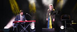 Na scenie widoczne są dwie osoby - wokalistka stojąca przy mikrofonie i po lewej stronie pianista. Wokalistka podczas robienia zdjęcia wykonywała utwór ukraiński. 