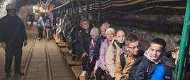 Uczniowie klasy 4 jadą wagonikiem górniczym w Kopalni Soli w Bochni, po lewej widoczny górnik