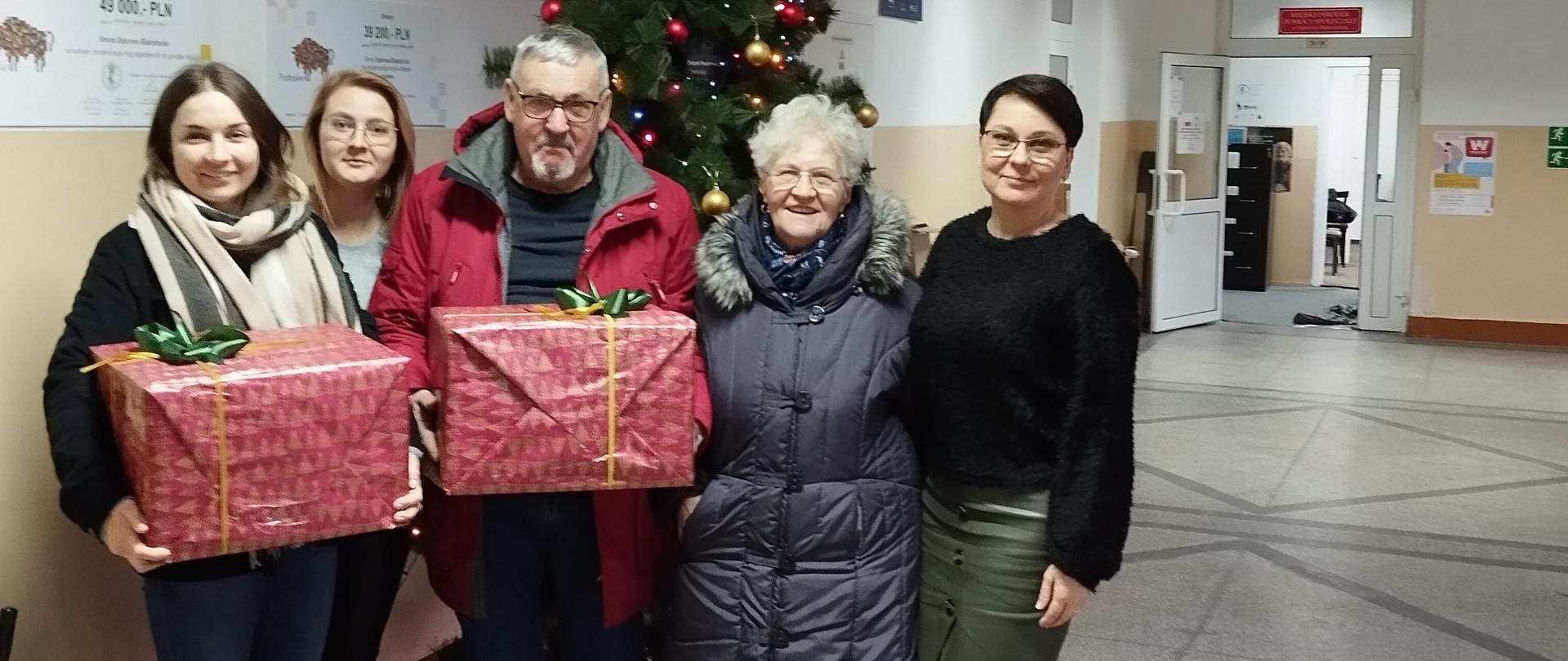 członkowie klubu senior+ wraz z kierownikiem ośrodka pomocy społecznej pozują z paczkami na tle choinki