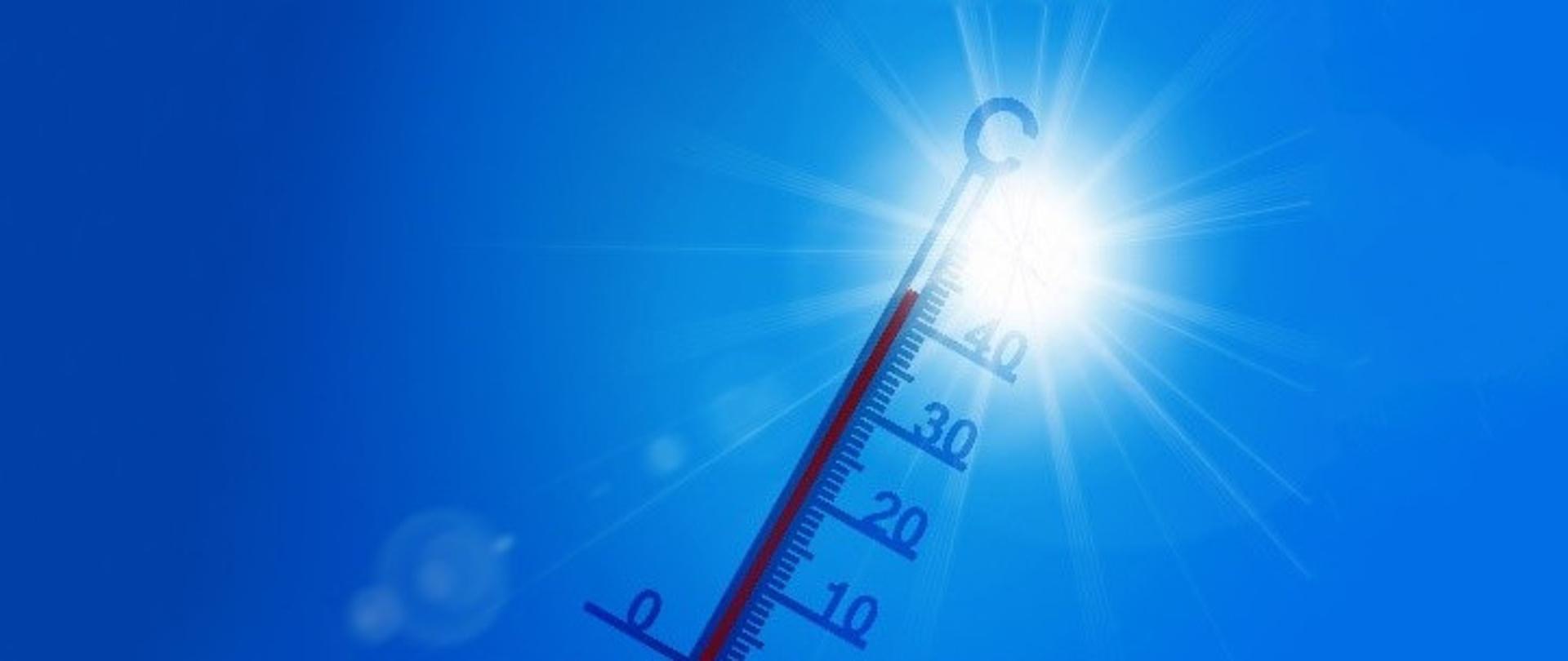Na tle niebieskiego nieba i słońca termometr rtęciowy wskazujący ponad 40 stopni Celsjusza