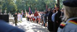 Uczestnicy uroczystości, poczty sztandarowe oraz warta wojskowa zgromadzeni na placu przed pomnikiem i kaplicą na cmentarzu.