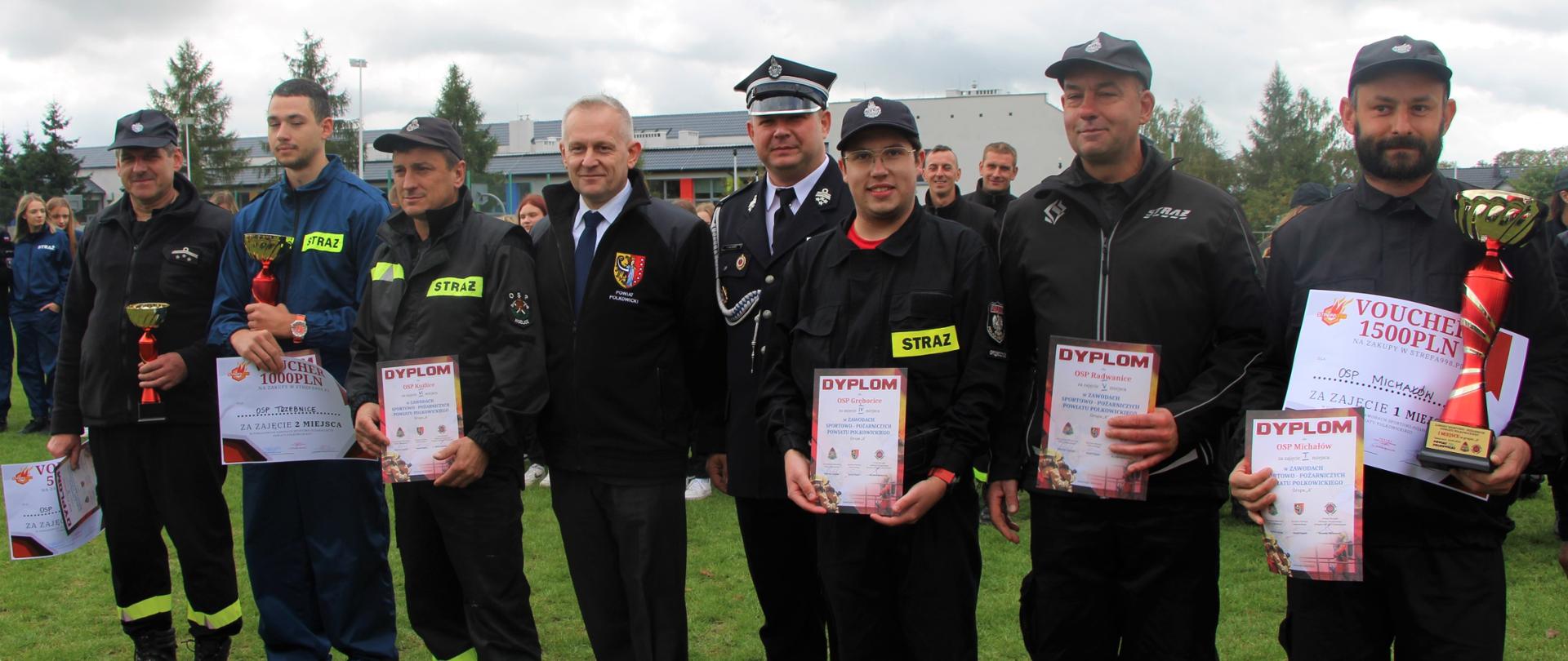 Władze powiatu polkowickiego pozują do zdjęcia ze strażakami na zawodach strażackich 
