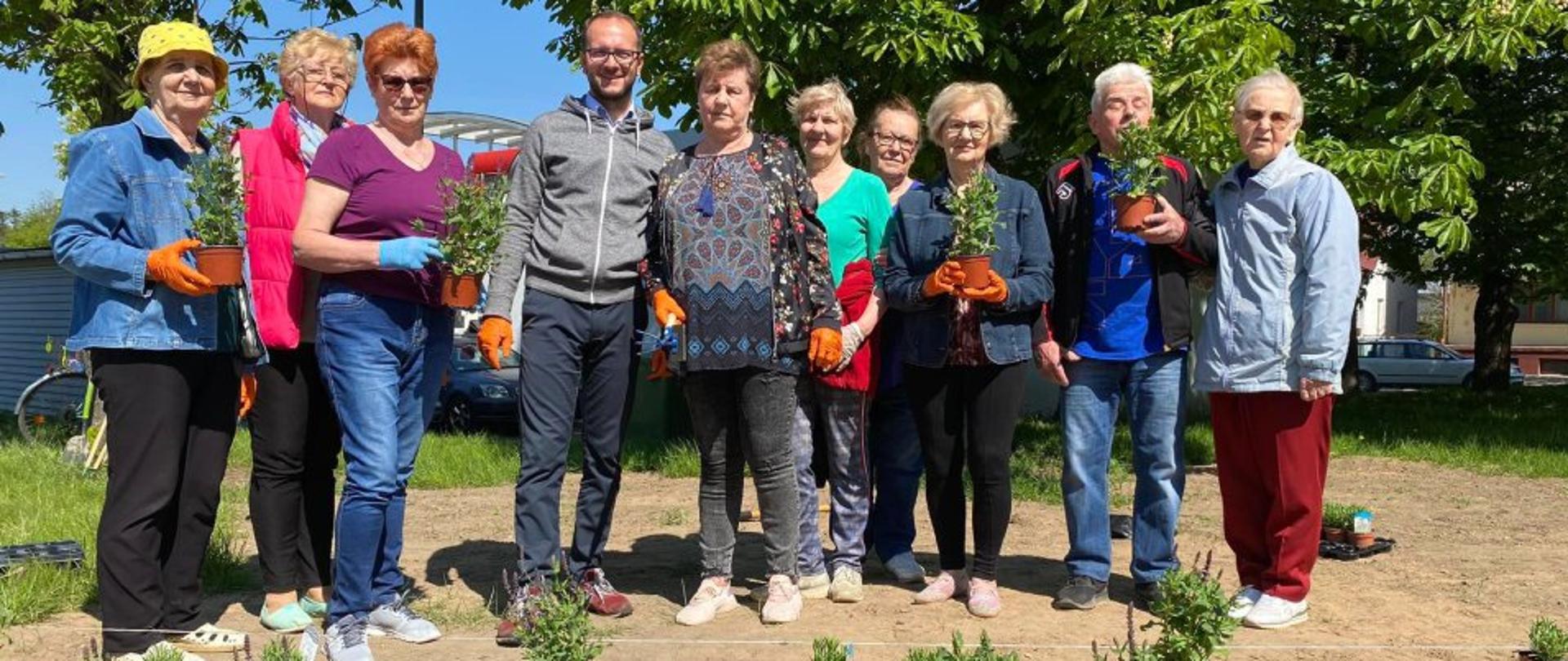 Seniorzy wraz z Burmistrzem Dąbrowy Białostockiej pozujący do zdjęcia z sadzonkami kwiatów