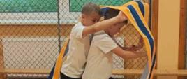 Dwóch uczniów jeden za drugim idą wewnątrz sportowej taśmy tworzącej koło
