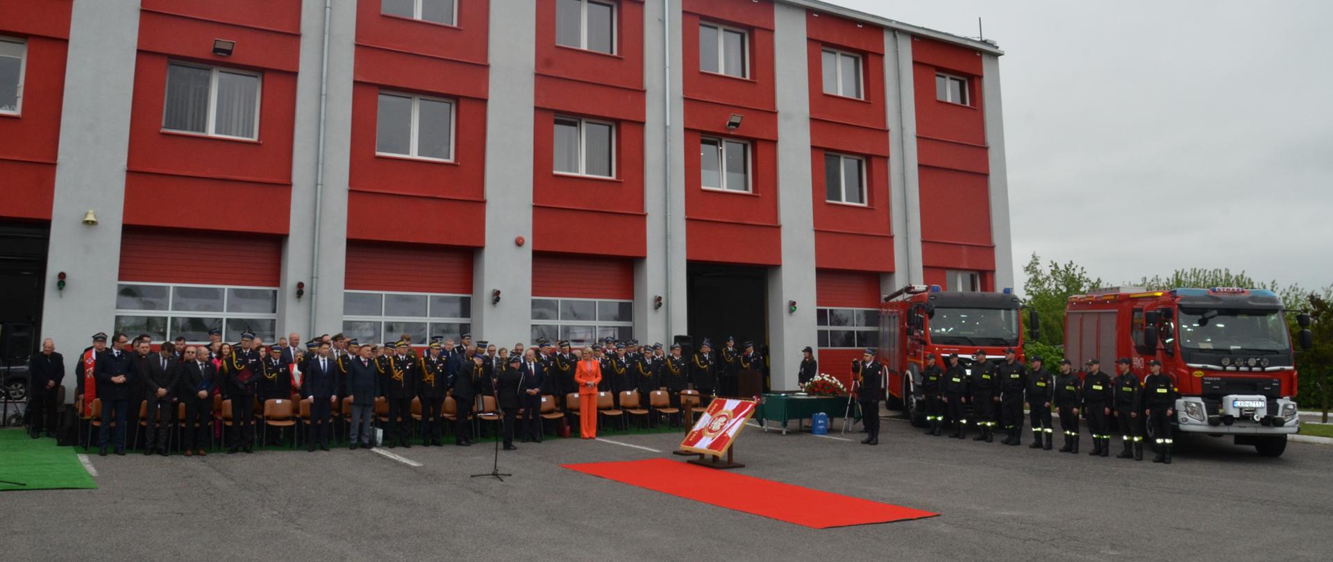 Na zdjęciu widoczny jest budynek Państwowej Straży Pożarnej w Kraśniku. Przy budynku zebrani są goście oraz wozy strażackie ze strażakami.