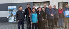 Grupa osób stoi przed budynkiem . W tle widoczny jest baner promujący Miasto i Gminę Zakliczyn. Część osób trzyma dokument, a cała grupa pozuje do wspólnego zdjęcia na zewnątrz.