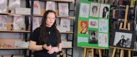 Zuzanna Kamińska podczas XVIII Wieczoru Twórczości Młodych. W tle na sztalugach prace Julii Rospond