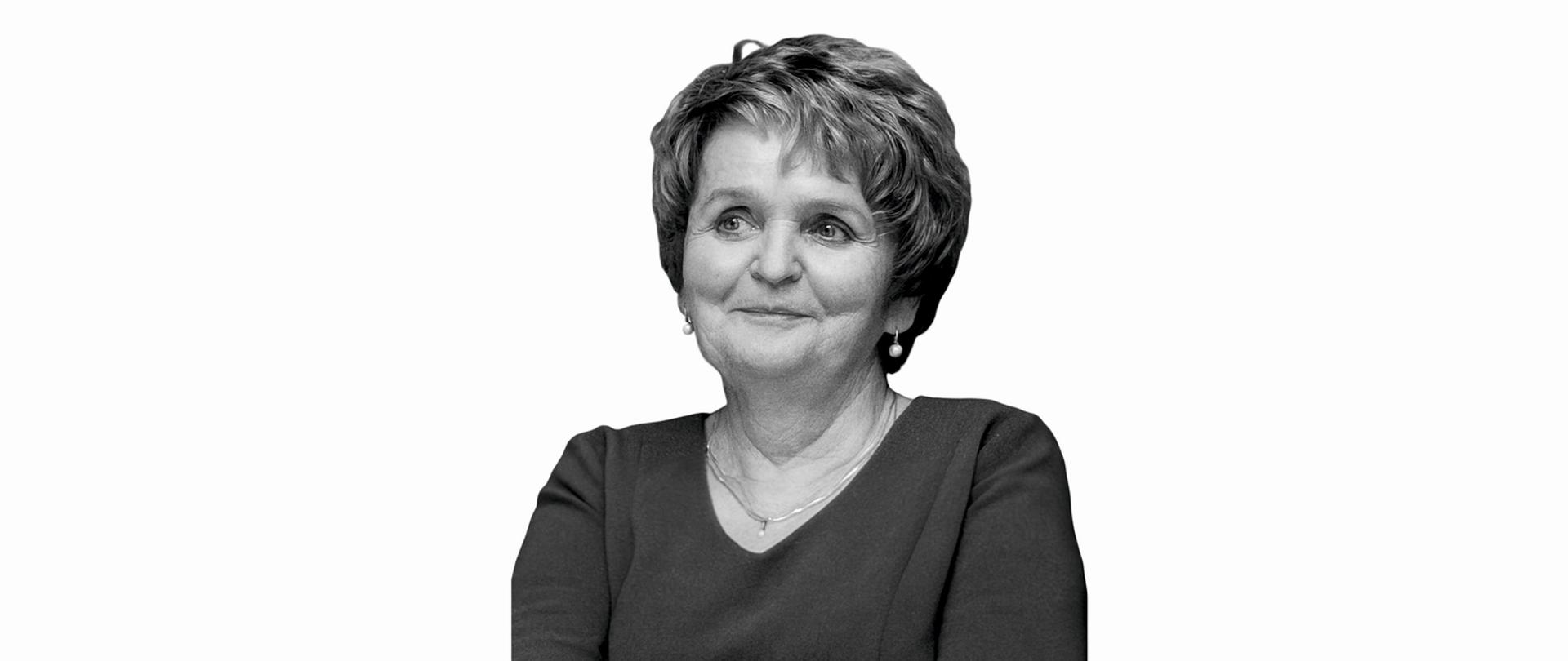 Kobieta w średnim wieku, krótko ostrzyżona, uśmiecha się lekko, ubrana w ciemną bluzkę, na białym tle.