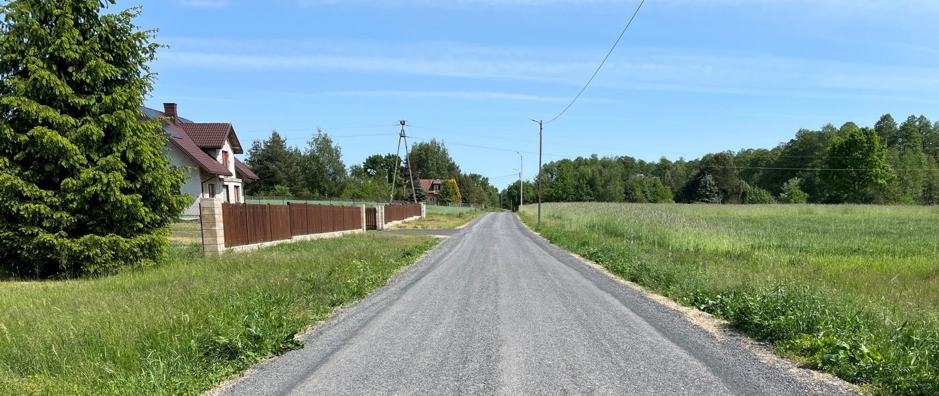 Powierzchniowo utrwalona droga gminna w miejscowości Nowa Wieś, po lewej stronie dwa domy. 