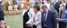 Reprezentacja Powiatu od lewej radna Rady Powiatu Sokołowskiego Urszula Krzymowska, starosta sokołowski Elżbieta Sadowska i wiceprzewodniczący Rady Powiatu Sokołowskiego Andrzej Kietliński niosą dar w postaci puszki na komunikanty, w tle widać wieńce dożynkowe