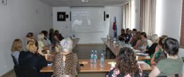 Uczestnicy konferencji siedzą przy biurku, przy monitorze zdalnym
