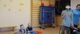 Podczas zajęć - prowadząca zajęcia zawiązała oczy jednemu dziecku celem przeprowadzenia ćwiczeń. Pozostałe dzieci siedzą na matach