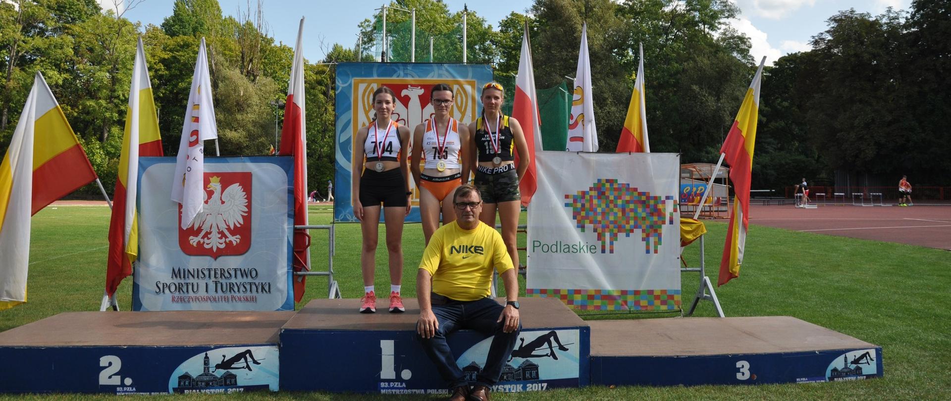 Trener pozuje do zdjęcia ze swoimi podopiecznymi, stojącymi na podium