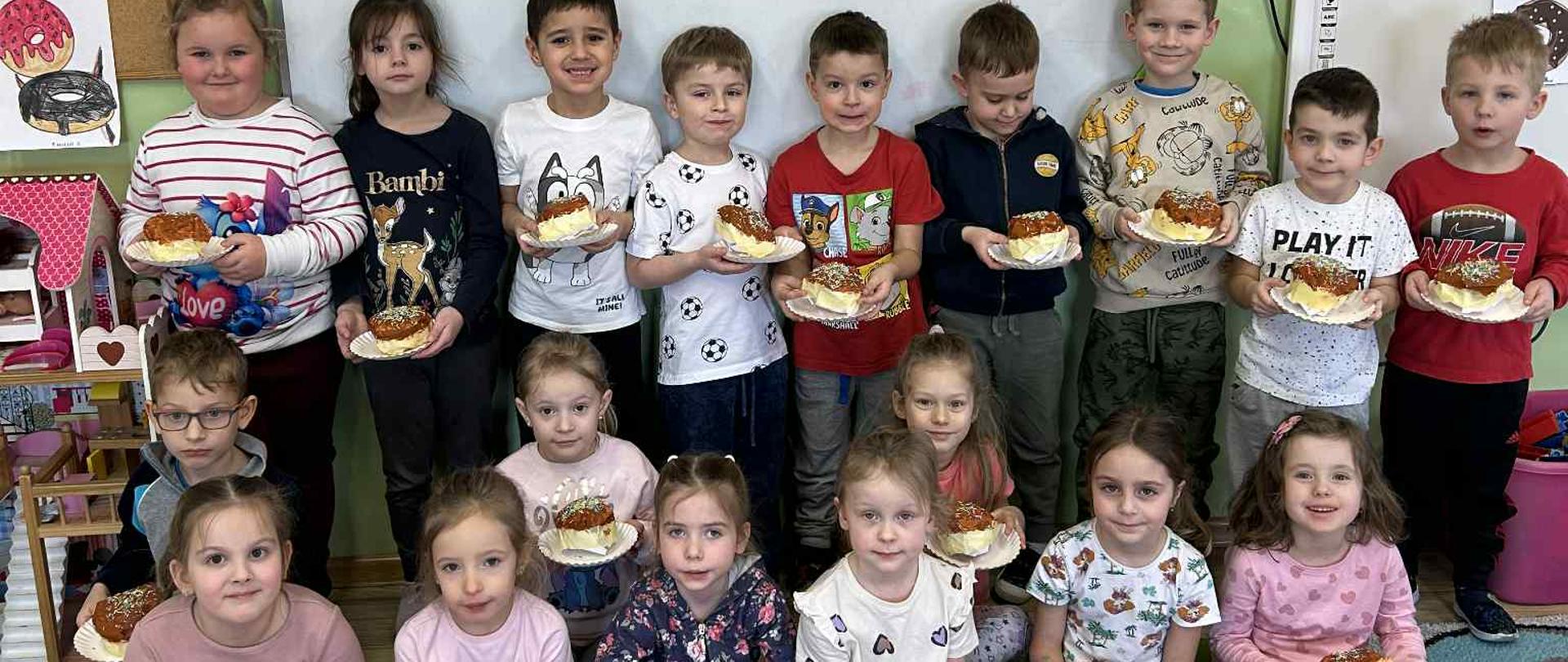 Grupa dzieci eksponuje wykonane prace plastyczne z okazji Tłustego Czwartku