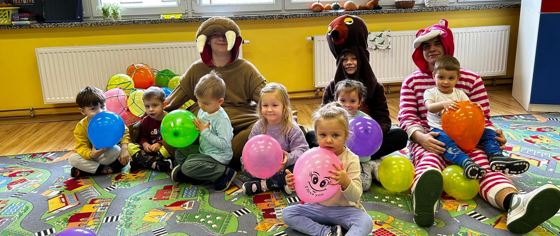 Przedszkolaki z kolorowymi balonikami przytulają się do maskotek.