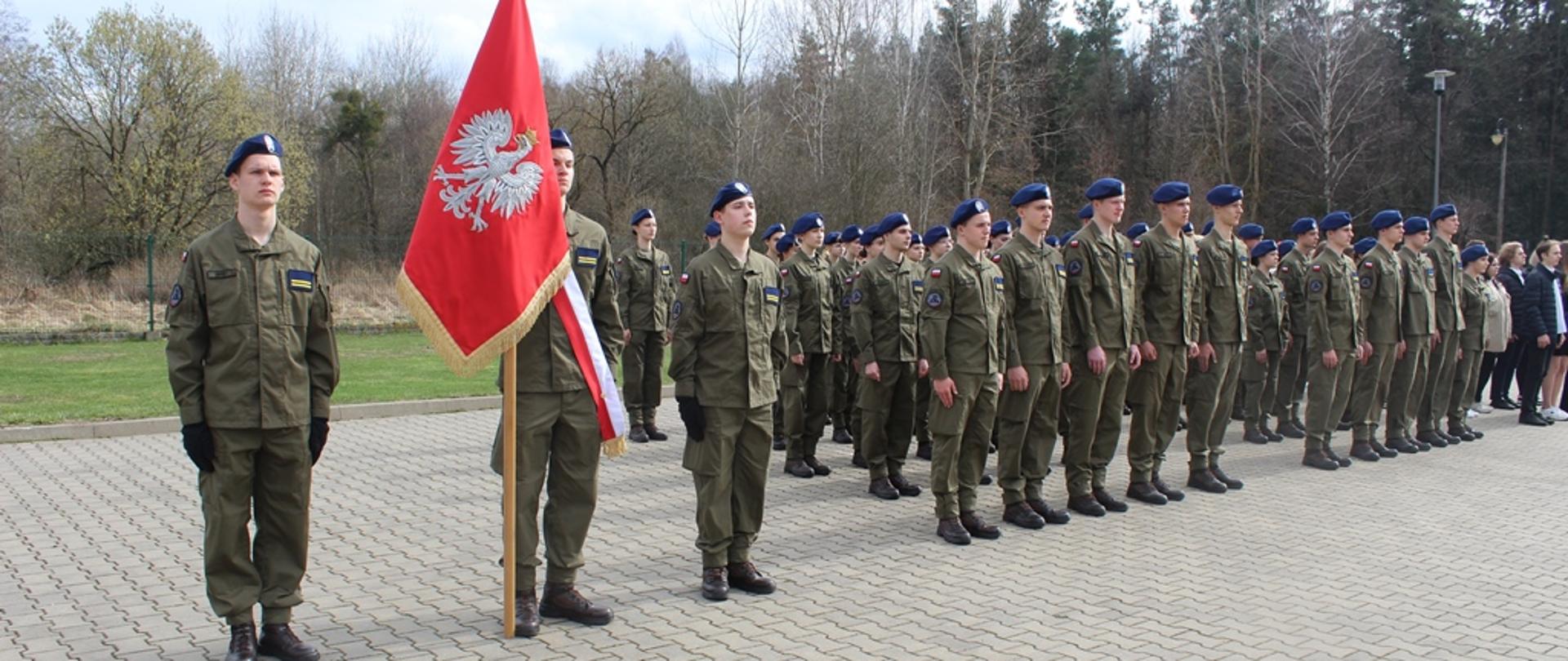 Uczniowie Oddziału Przygotowania Wojskowego stoją w szeregu ze sztandarem