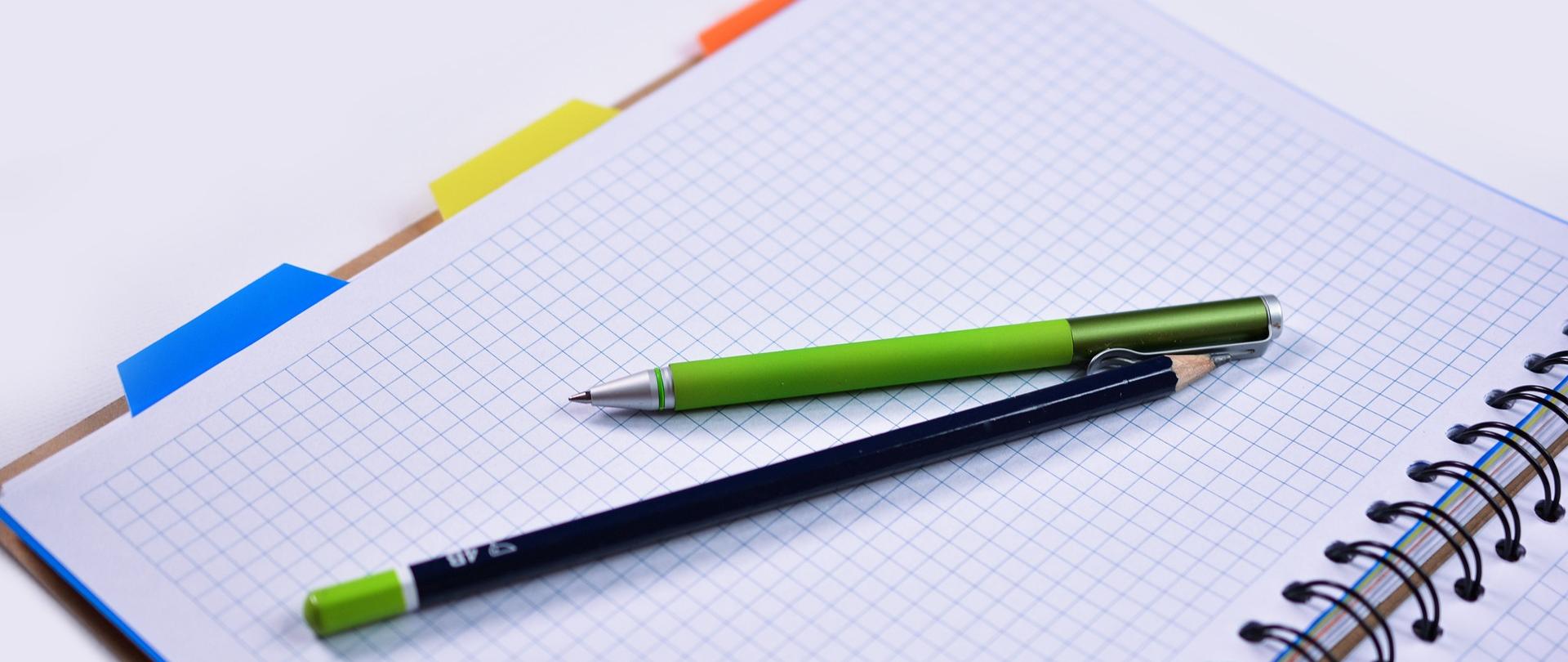 Długopis i ołówek położone na otwartym notatniku w kratkę z kolorowymi zakładkami