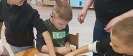 Wspólne pieczenie pierniczków - dzieci siedzą przy stole i wykonują czynności związane z przygotowaniem ciasteczek. Pozują przy tym do zdjęć