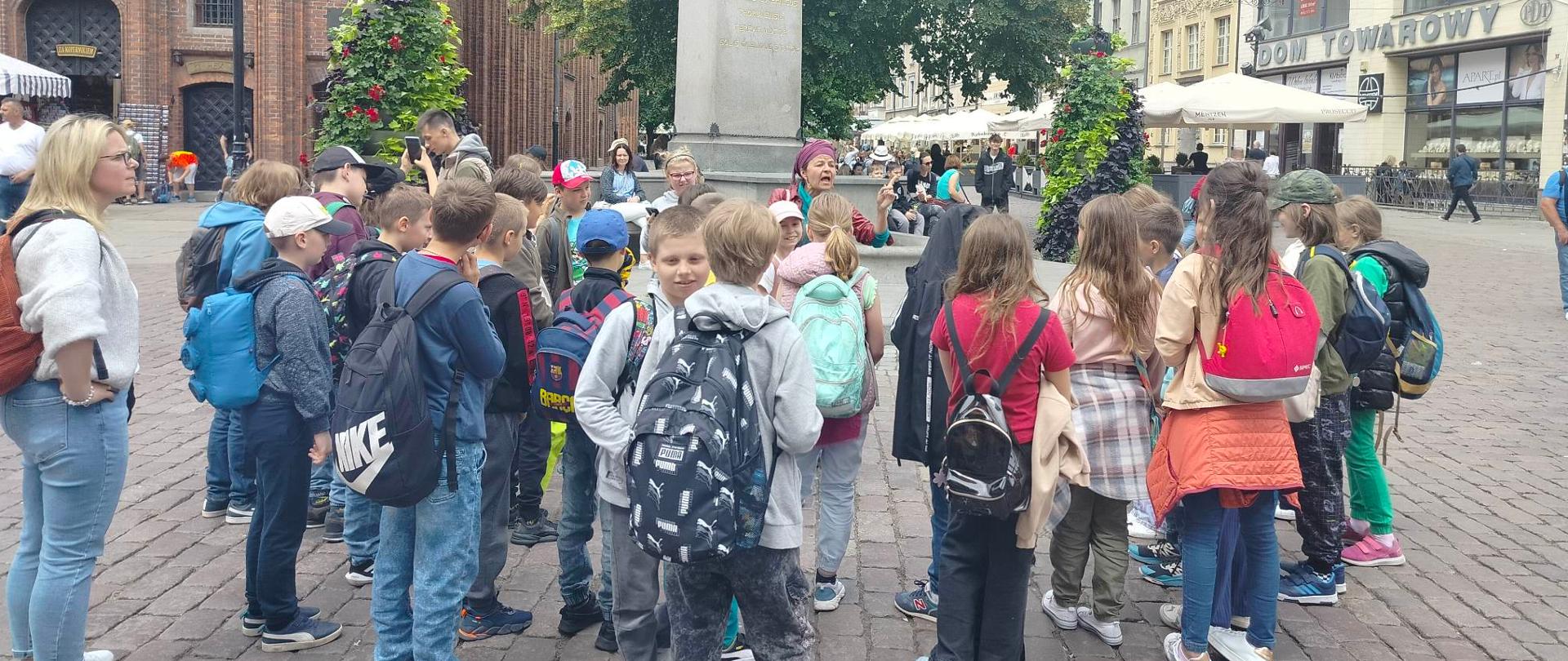 Dzieci ustawione na rynku wokół pomnika Mikołaja Kopernika