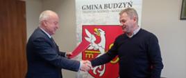 Dwie osoby stoją podają sobie ręce i przekazują podpisaną umowę