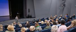 Uczestnicy konferencji w sali Centrum Kultury i Wypoczynku w Proszowicach podczas spotkania, na głownej scenie jeden z prelegentów 