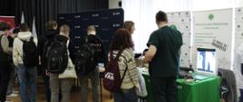Stoiska promocyjne przygotowane przez uczelnie. Przy stoiskach stoją uczniowie, rozmawiają z przedstawicielami uczelni