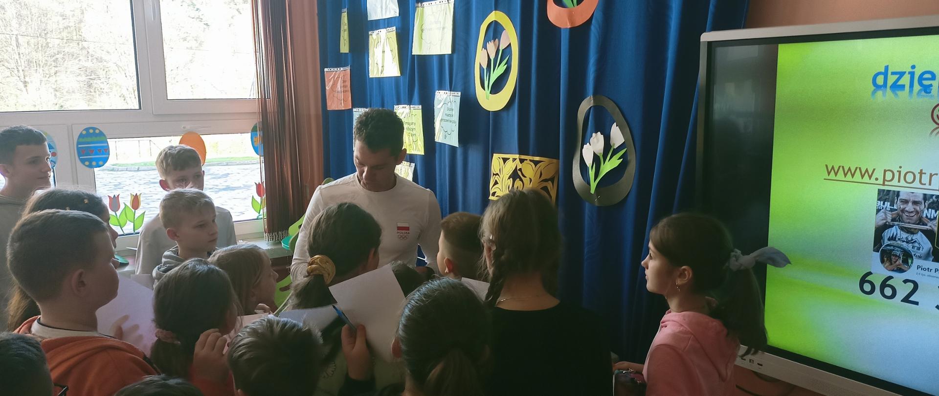 Mistrz w biegach przeszkodowych pan Piotr Prusak rozdaje autografy otaczającym go uczniom