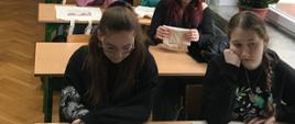 Uczennice siedzą w ławkach, oglądają otrzymane torby