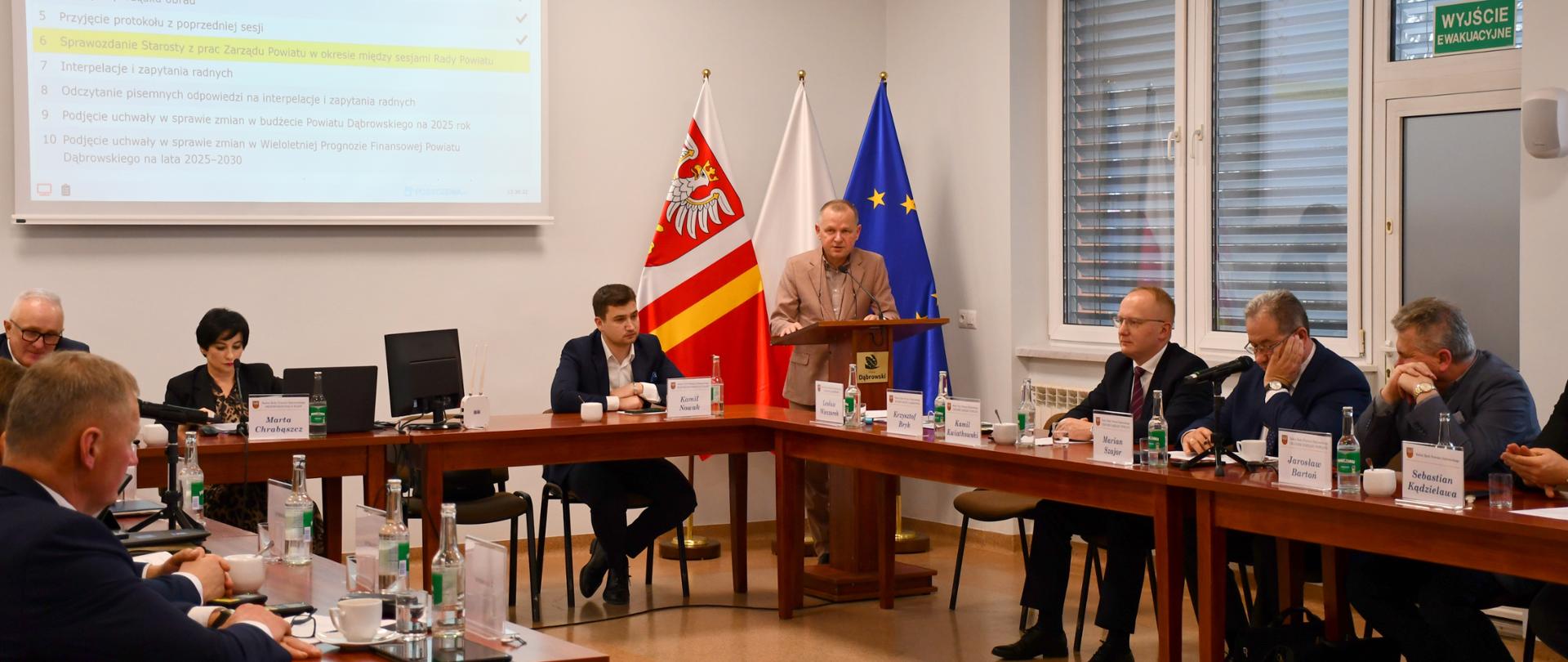 Starosta Dąbrowski zabiera głos przy mównicy, a radni siedzą przy stołach