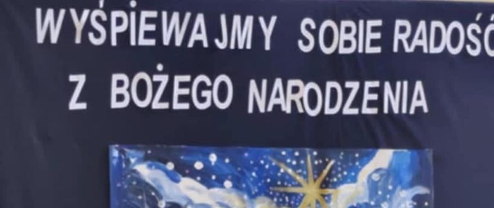 Emilka w beżowym komplecie z dyplomem w ręku stoi na tle dekoracji świątecznej.