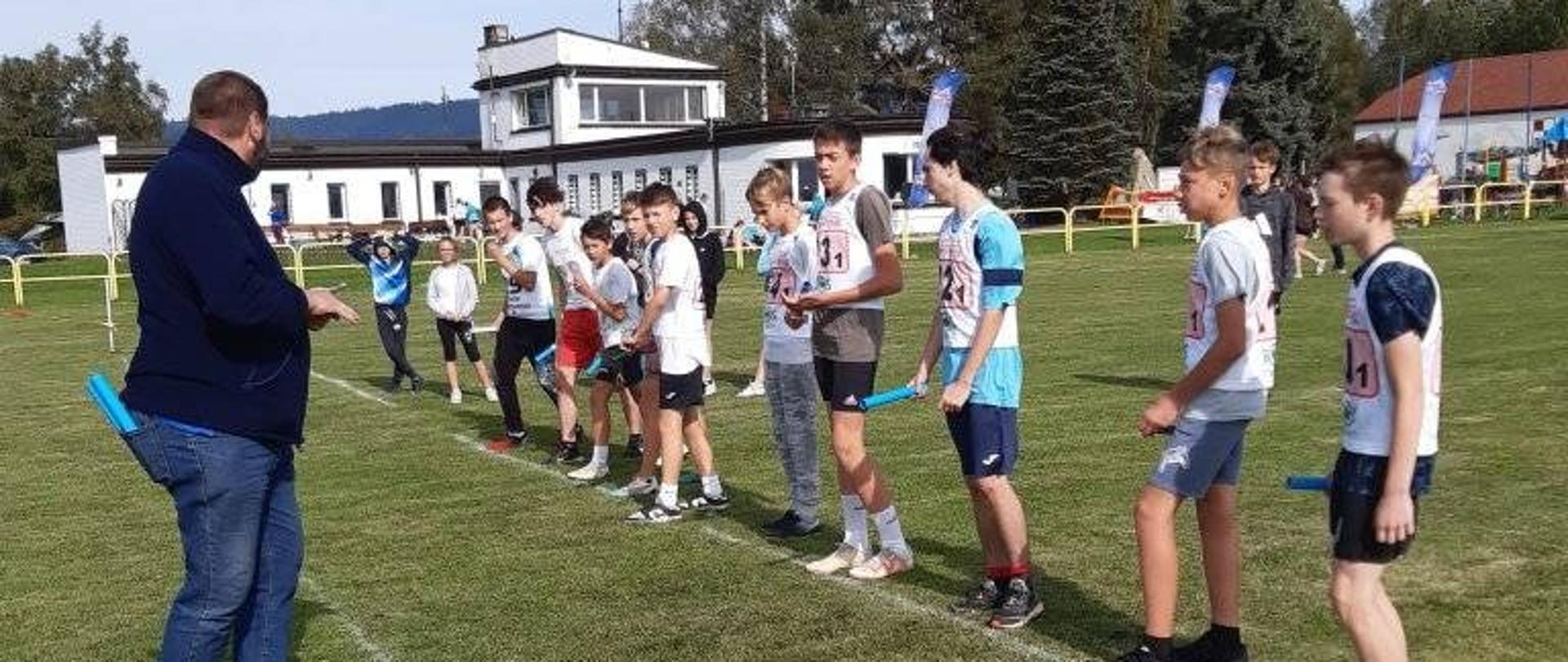 Uczniowie ustawieni na linii startu sztafetowych biegów przełajowych. 