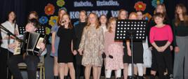 dziewczynki stoją na scenie i śpiewają jeden chłopak siedzi i gra na akordeonie 