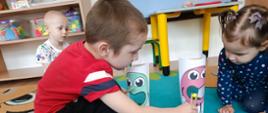 Zabawy z kropkami - chłopiec trzyma w ręku drewnianą pęsetę z kolorowym groszkiem