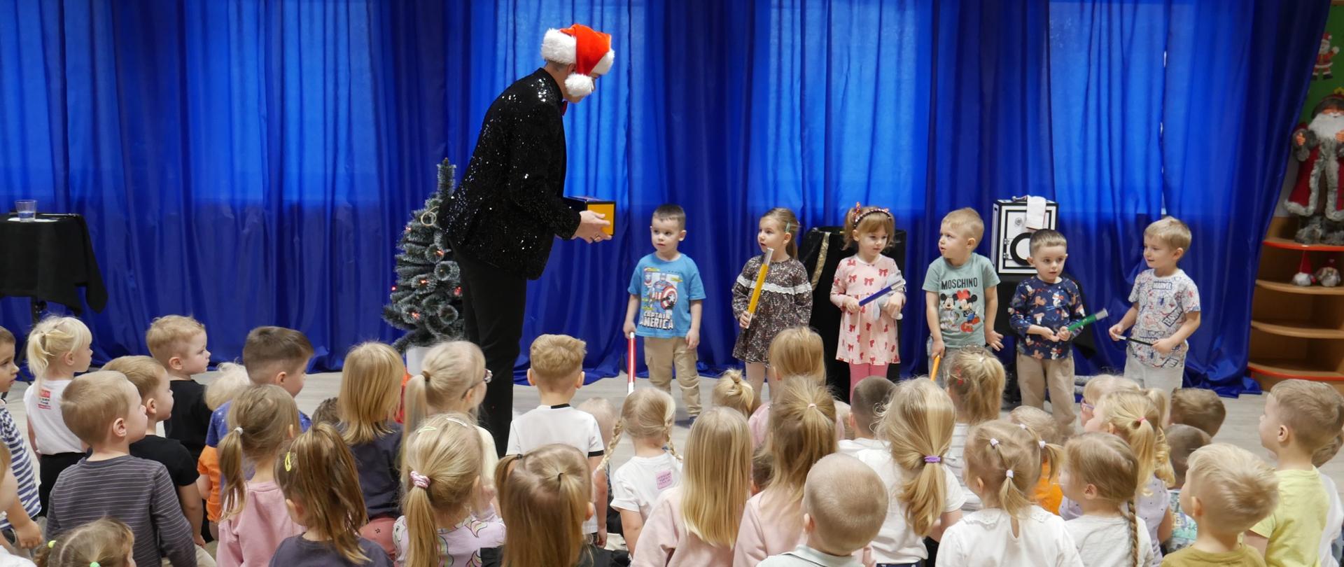 1 dorosły magik i 6 dzieci, przed nimi grupa dzieci 