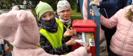Dzieci wrzucają kartki pocztowe do czerwonej skrzynki na listy