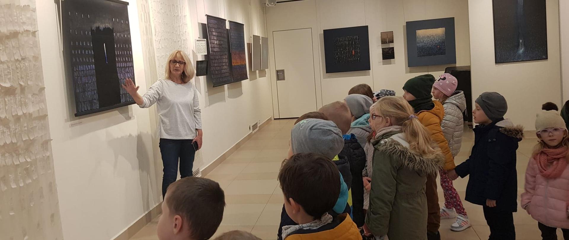 Grupa dzieci ogląda pokazywany przez przewodnika obraz