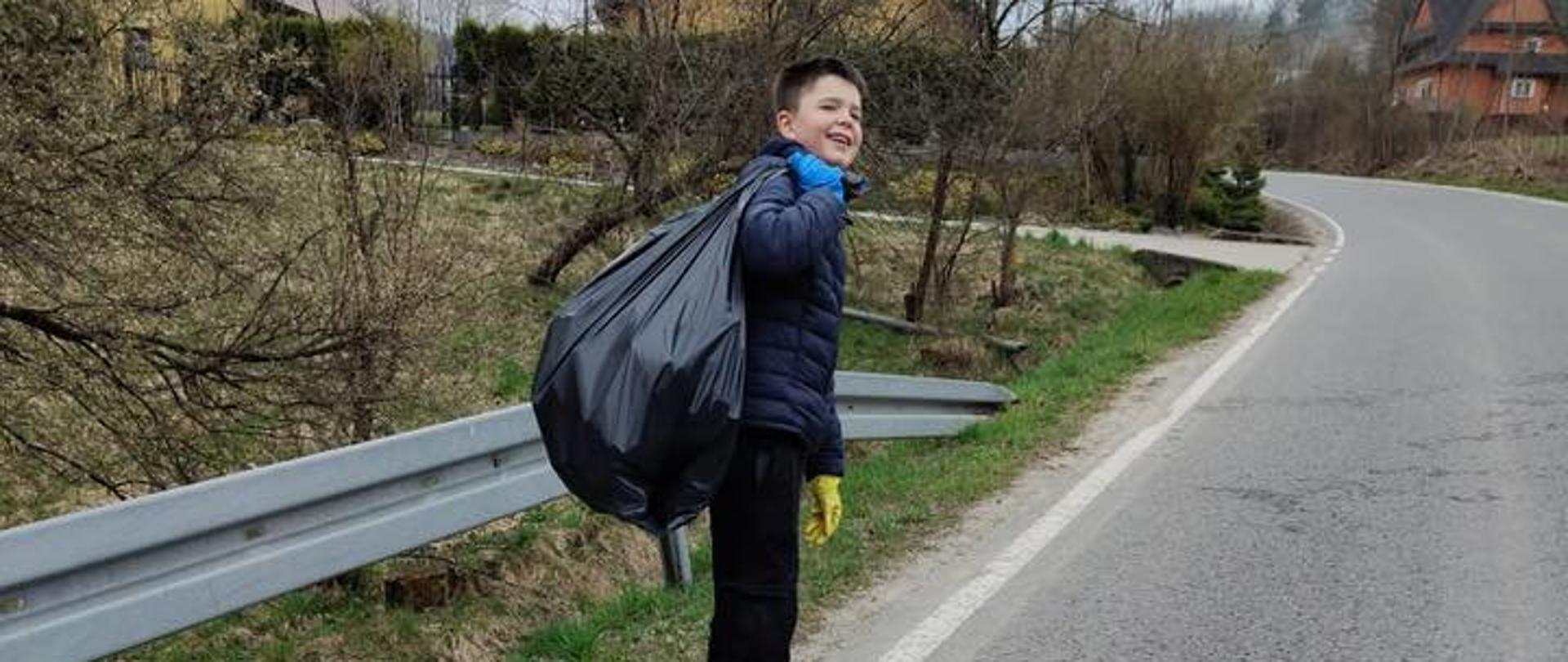 Uczeń trzyma na plecach czarny worek z zebranymi śmieciami