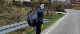 Uczeń trzyma na plecach czarny worek z zebranymi śmieciami